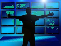Bild zeigt einen schattierten Mann, der vor einer Tastatur und vielen Bildschirmen steht, die Hände ausstreckt